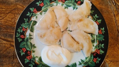 Talerz, na którym leży siedem pierogów ze skwarkami.