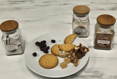 Ciasta i kawałki orzechów leżące talerzu, obok talerza stoją trzy szklane pojemniczki z przyprawami. 