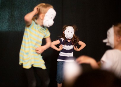 Dzieci w białych maskach na scenie.