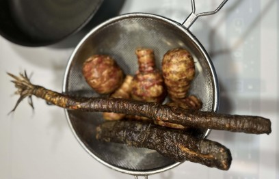 Klika warzyw bulwiastych i dwa warzywa podłużne leżą w metalowym sitku. 