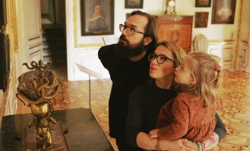 Mężczyzna oraz kobieta z dzieckiem na ręku zwiedzają pomieszczenie Pałacu Myślewickiego. 