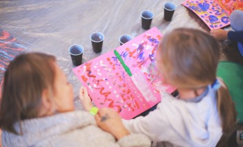 Dzieci siedzące na podłodze przed kolorowym obrazkiem. 