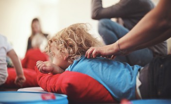 Dziecko leżące na podłodze. Na plecach dziecka opiera się kobieca dłoń. 
