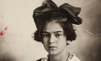Portret młodej dziewczyny z dużą kokardą na głowie, ubranej w białą i czarną bluzkę, z naszyjnikiem na szyi. 