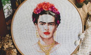 Haftowany portret Fridy Kahlo, naciągnięty na okrągłą obręcz. Wokół leżą haftowane serwetki. 