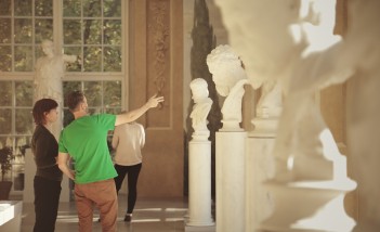 Grupa osób ogląda białe, marmurowe rzeźby w Królewskiej Galerii Rzeźby w Łazienkach Królewskich. 