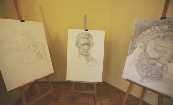 Trzy sztalugi z rysunkami stojące obok siebie. 