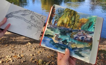 Kobiece dłonie trzymają dwa rysunki na tle wody w stawie: z lewej strony rysunek gałęzi wykonany ołówkiem, z prawej pejzaż namalowany farbami.