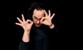 Mężczyzna ubrany na czarno trzyma uniesione ręce przy twarzy.