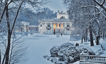 Pałac na Wyspie w zimowym otoczeniu. Budynek Pałacu i pobliskie drzewa pokrywa śnieg.
