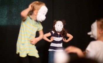 Dzieci w białych maskach na scenie.