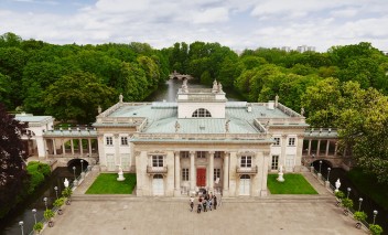 Widok na Pałac na Wyspie w otoczeniu drzew i wody. 