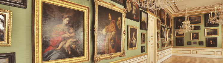 Galeria Obrazów w Pałacu na Wyspie. Obrazy z kolekcji króla Stanisława Augusta w złotych ramach wiszą na jasnozielonej ścianie. Z sufitu zwisają trzy kryształowe żyrandole.